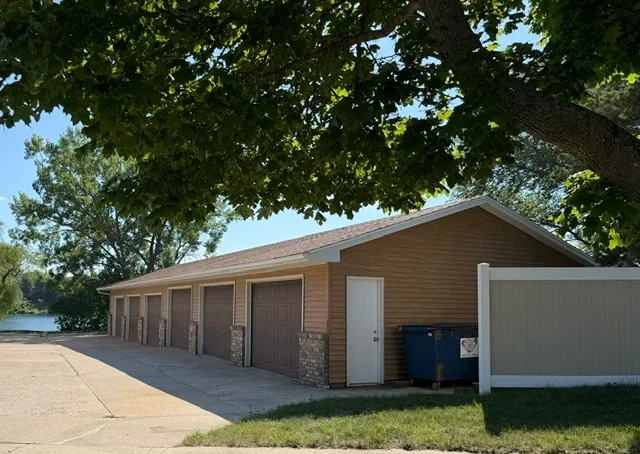 Brown garage with four doors and new asphalt shingle pitched roof, stone veneer base, concrete driveway