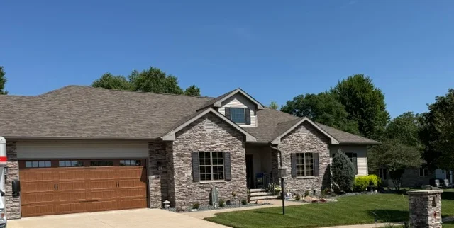 Gray asphalt shingle roof on stone and brick residential home with dormer and gable details