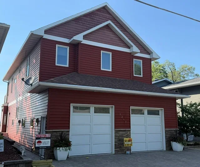 Two-story home with dark gray asphalt shingle roof, burgundy siding, white trim, and white garage doors